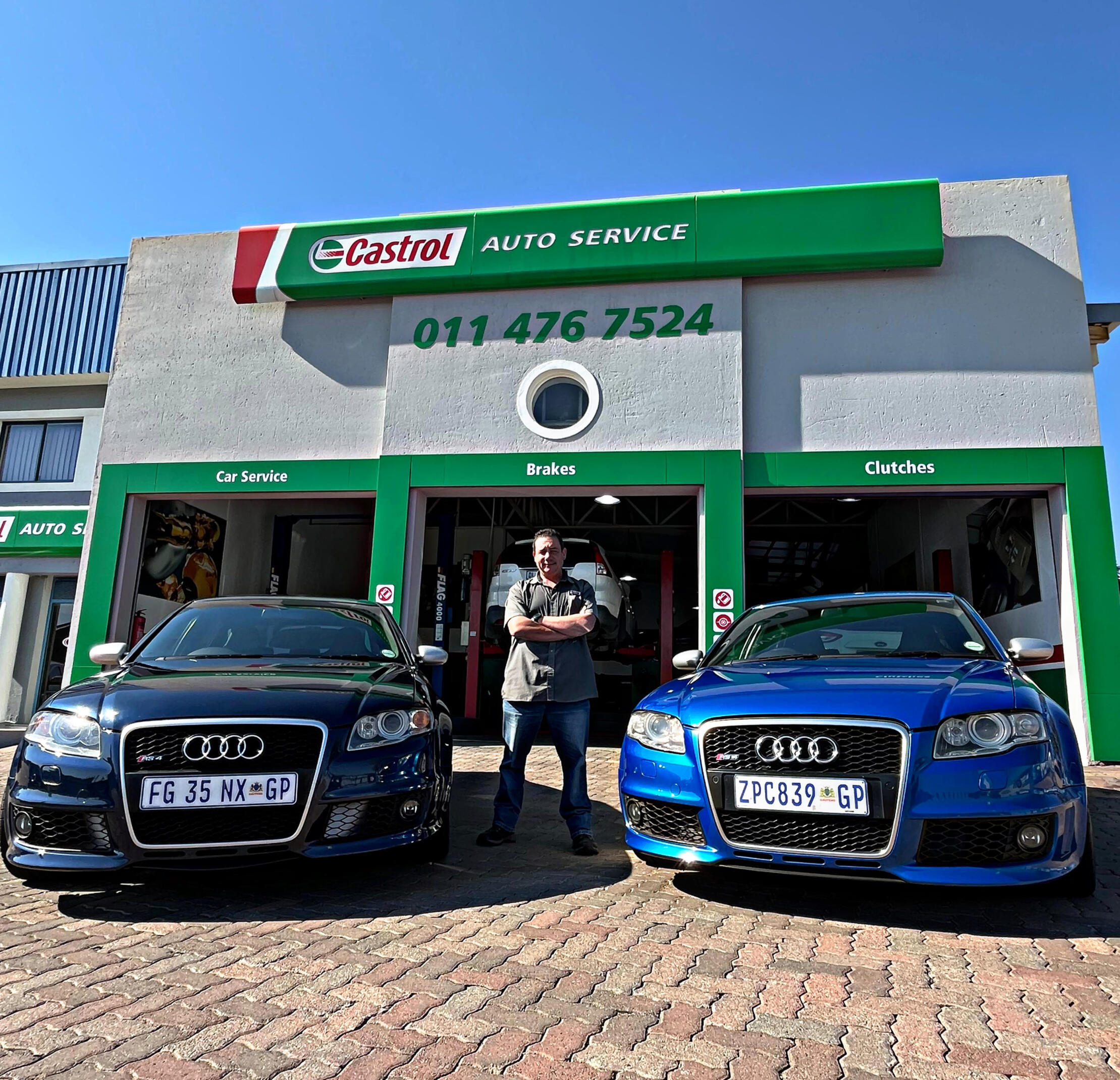 Manager Casper standing outside of the Castrol Auto Service Northcliff building, standing infront of the doors that have an RMI logo on them. The Castrol logo and "auto service" is large on the front of the building in green and red and white.